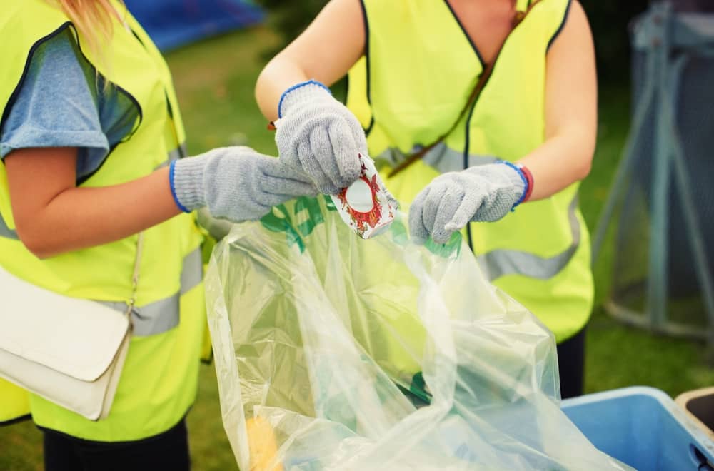 deux personnes bénévoles avec des gants et des gilets jaunes, ramassant des déchets durant un festival