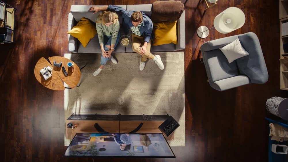 vue du ciel d'un couple sur son canapé regardant une émission avec Alain Chabat à la télévision