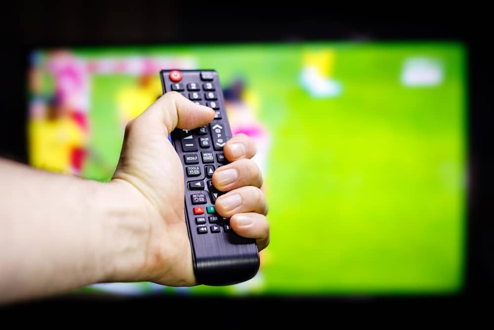 main d'un homme tenant une télécommande devant une chaîne locale de BFM