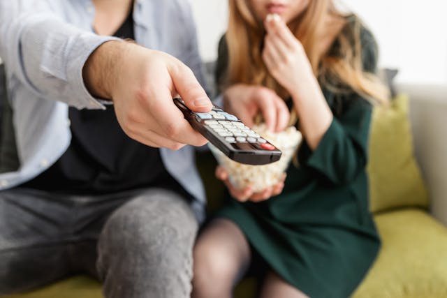 couple regardant un programme sur Outre-Mer la Première avec une télécommande et du popcorn