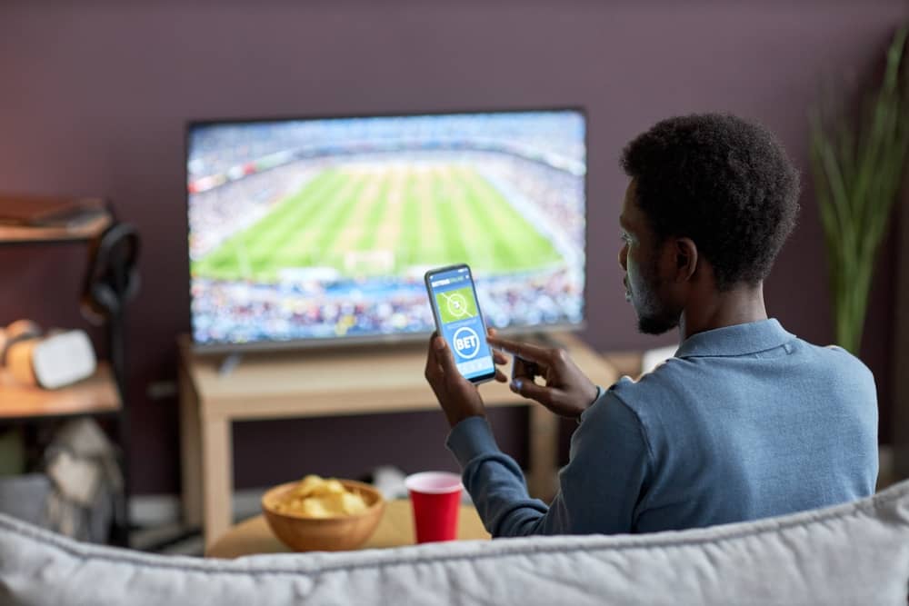 homme avec son smartphone en train de regarder TV7 à la télé