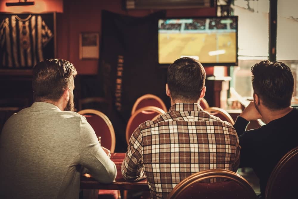 3 hommes regardant un événement sportif sur la chaîne locale TVR