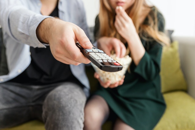 2 personnes regardant la télé avec des popcorns et une télécommande à la main