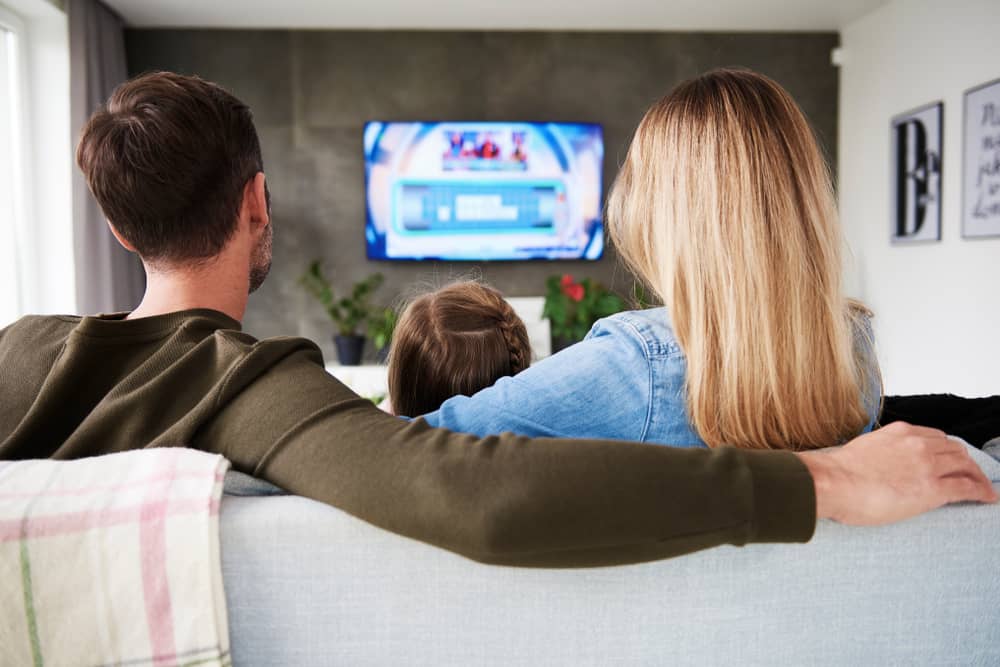 un couple et son enfant assis sur un canapé regardent TLMASMAD à la télévision