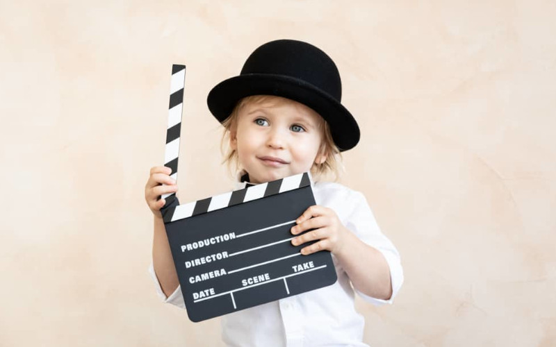 Petit enfant coiffé d'un chapeau avec un clap de tournage