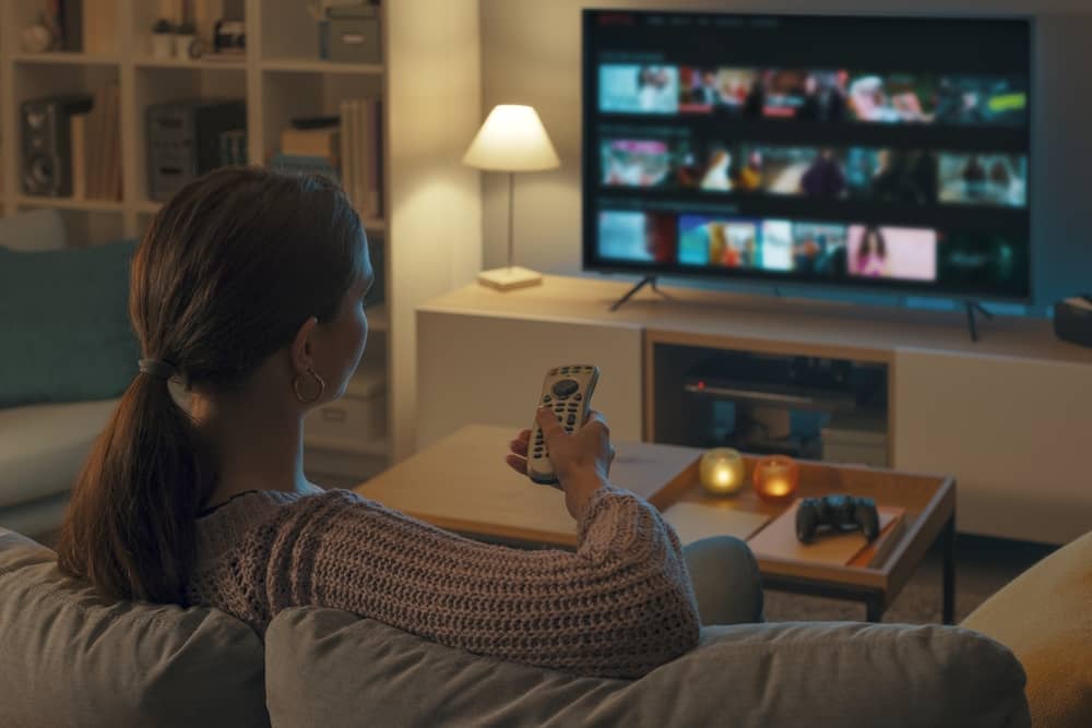 femme regardant la télé depuis sa console de jeux, avec une télécommande à la main